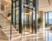 Luxury glass-enclosed residential elevator beside an illuminated staircase